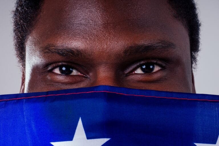african american man looking at camera and proudly holding american flag at studio