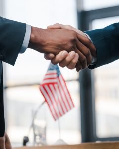 cropped view of multicultural diplomats shaking hands near flag of america